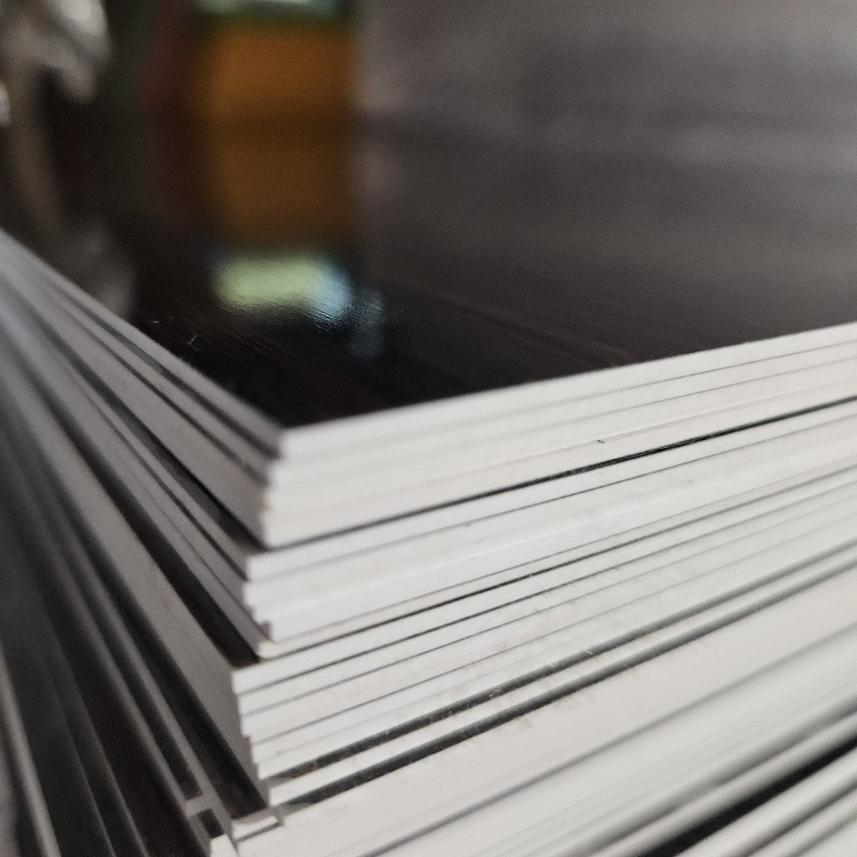 Stack of 1.5 mm two-tone engravable acrylic sheets showing the thin white core edge