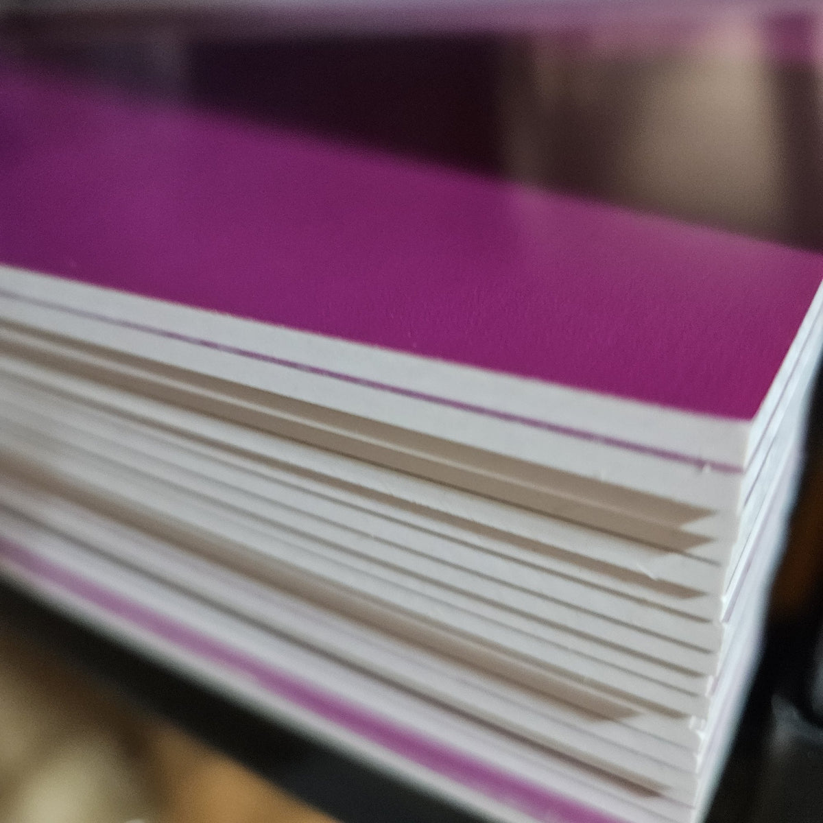 Stack of 3 mm (1/8 inch) purple two-tone engravable acrylic sheets showing the white core edge